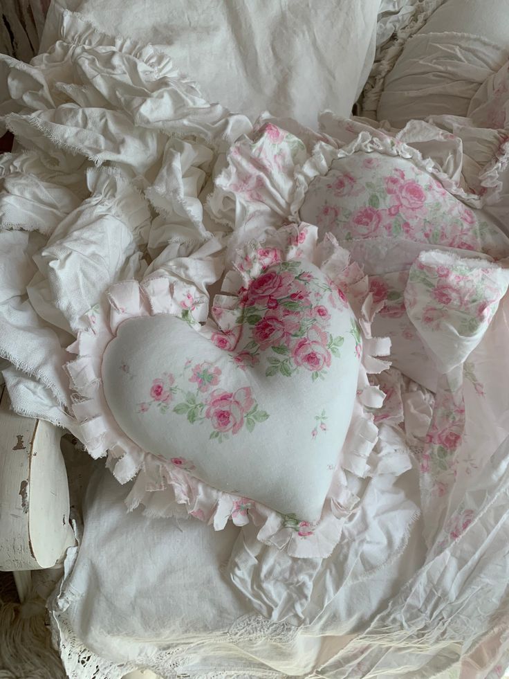 a heart shaped pillow sitting on top of a pile of white sheets and ruffles