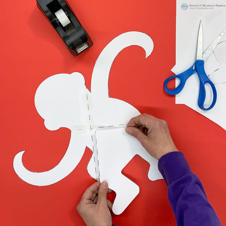 someone cutting out the shape of a monkey with scissors on a red surface next to some cut outs