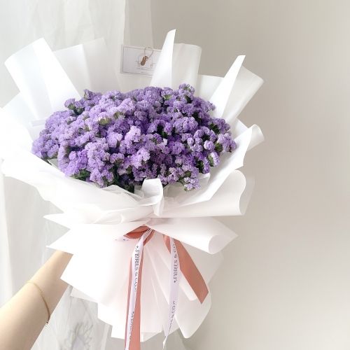 a person holding a bouquet of purple flowers in their left hand with a pink ribbon around it