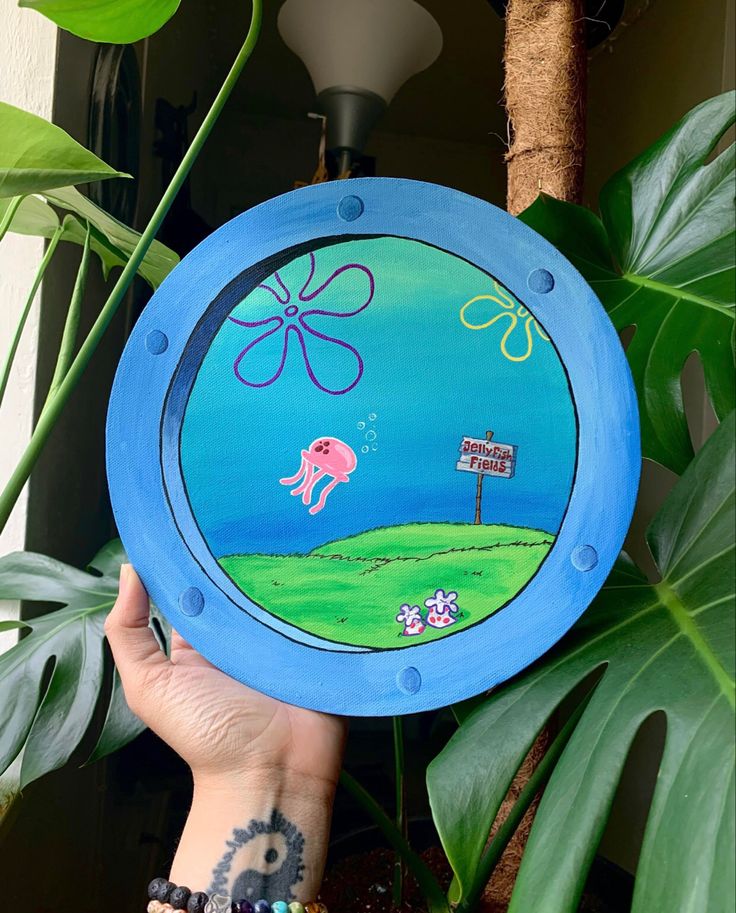 a hand holding up a painted plate with an elephant on it's side and a street sign in the background