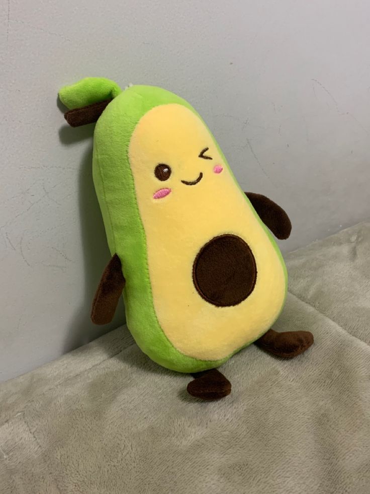 a green and yellow stuffed animal sitting on top of a white bedding sheet next to a gray wall