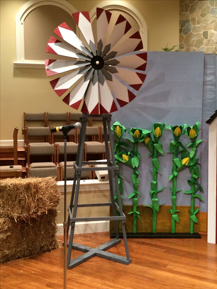 a windmill sitting on top of a wooden floor in front of a stage with hay bales