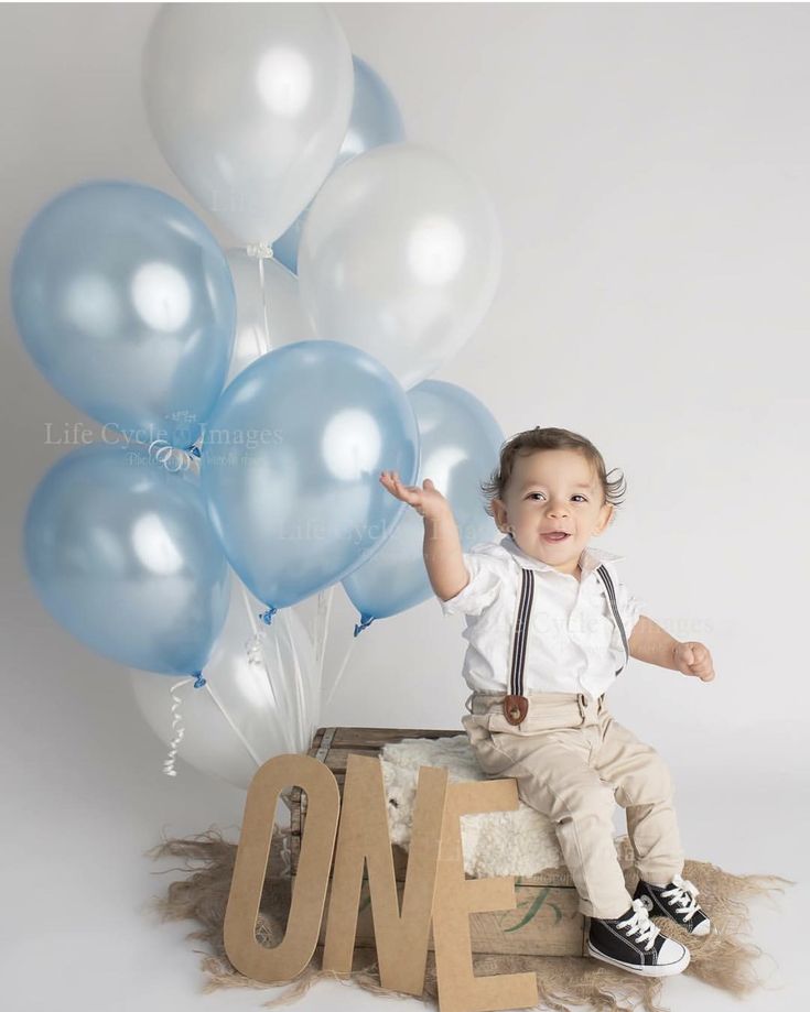 a little boy sitting on top of a box with balloons