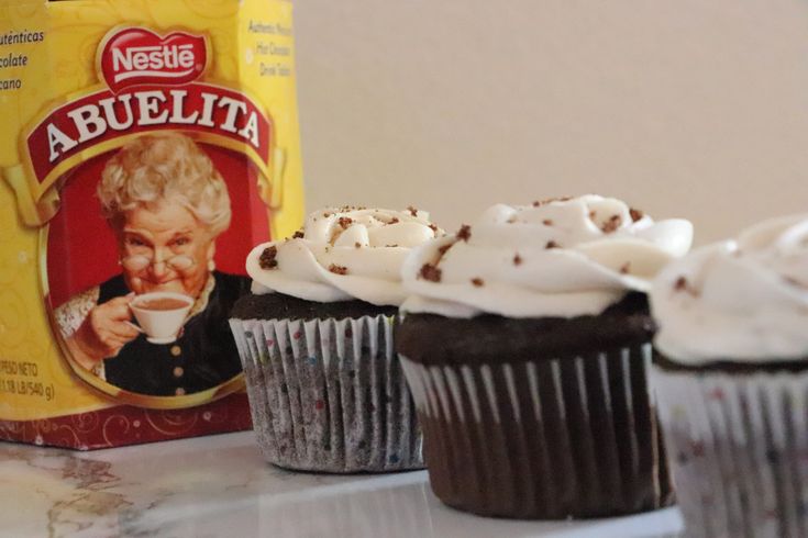 three cupcakes with frosting sitting on a counter next to a bag of coffee