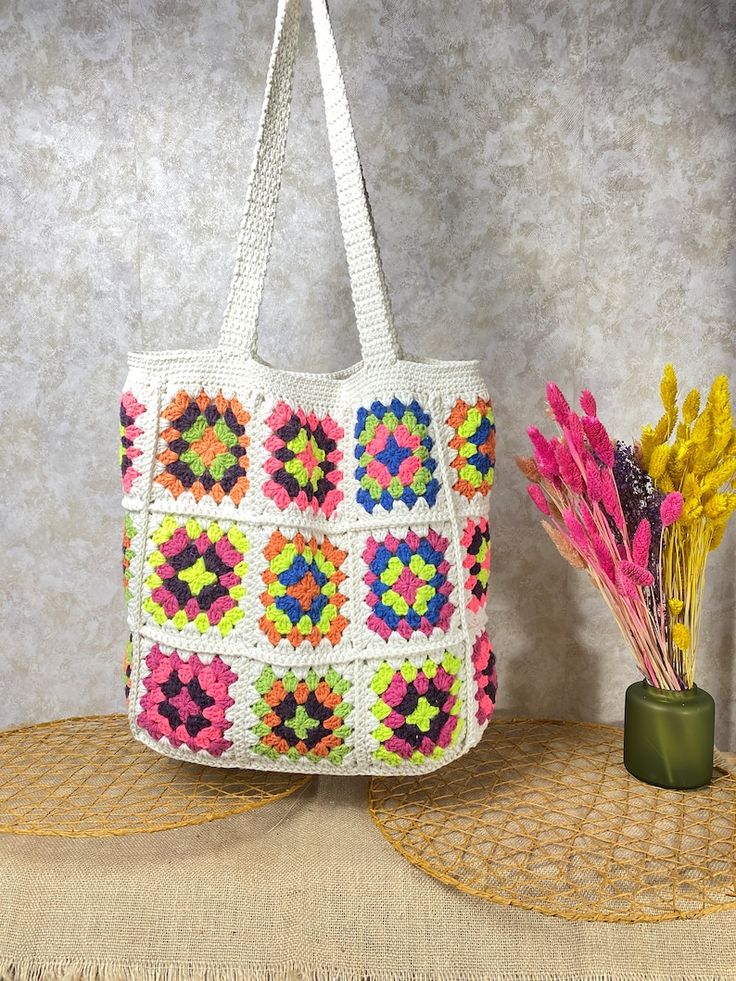 a crocheted bag sitting on top of a table next to a vase with flowers