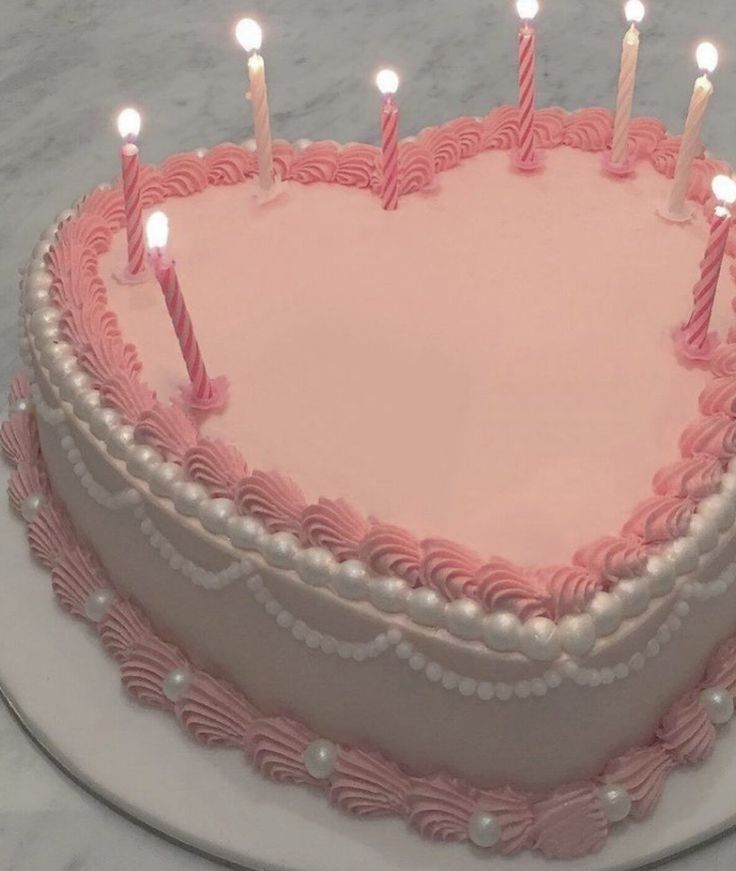 a pink heart shaped cake with candles on it's top and white frosting