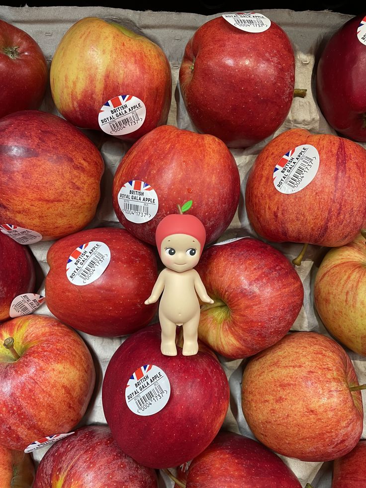 there are many apples with stickers on them and a small doll in the middle