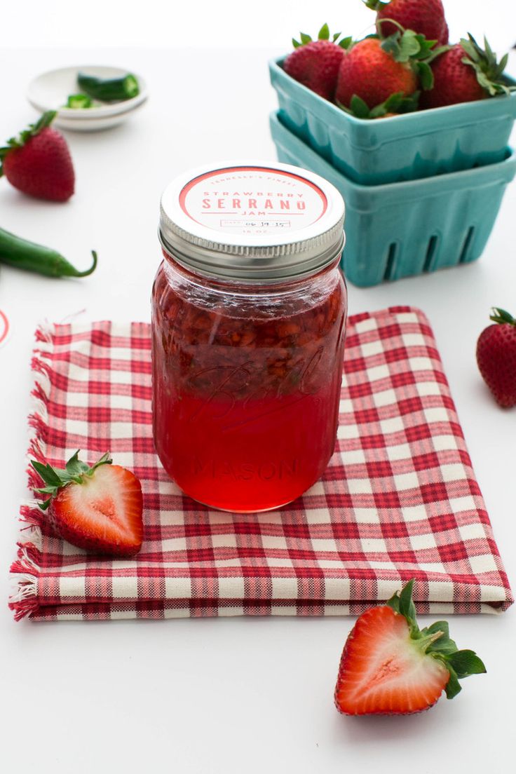 a jar of strawberry jam sitting on top of a red and white checkered cloth