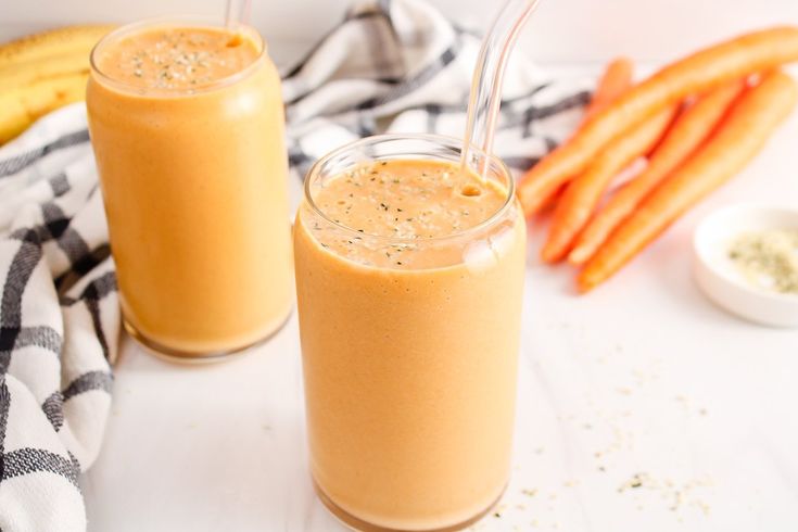 two glasses filled with smoothie next to some carrots