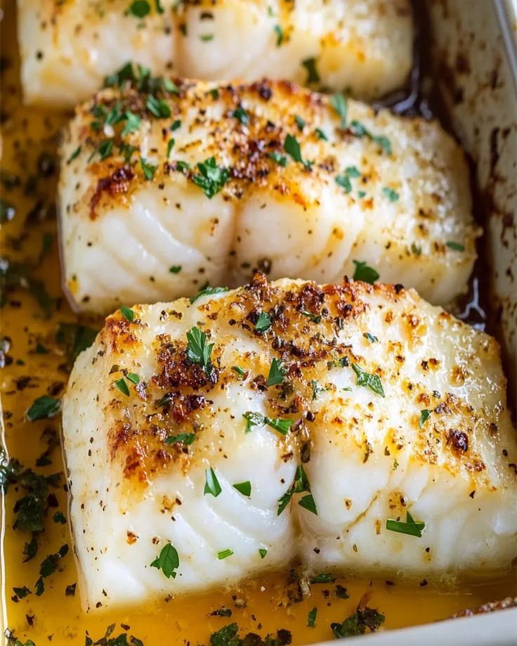 three fish fillets in a pan with mustard and parsley on top, ready to be cooked