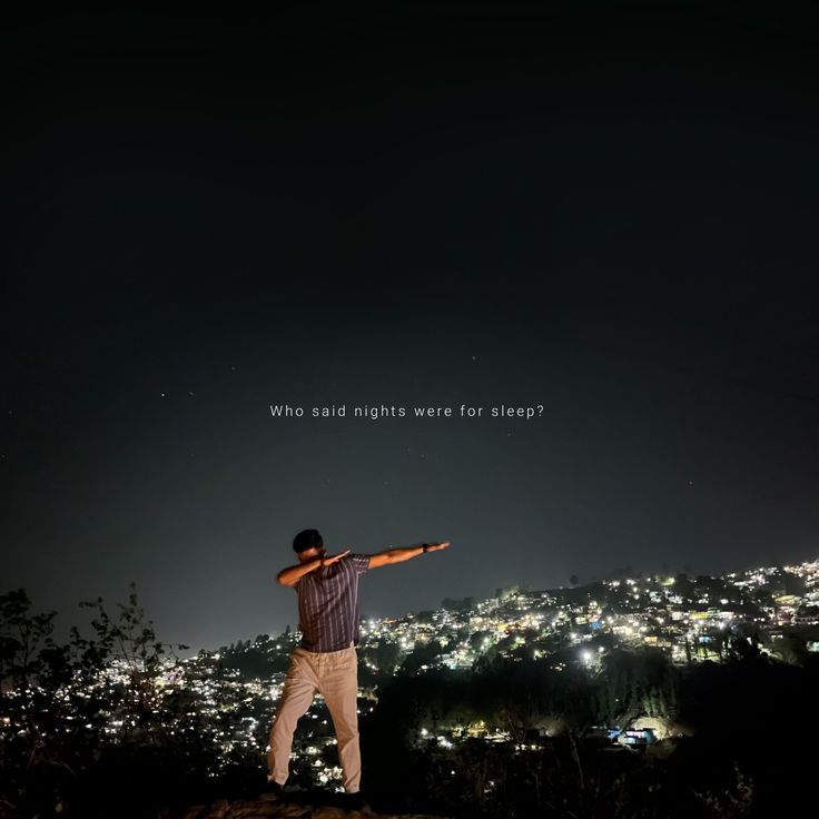 a man standing on top of a hill with his arms outstretched in front of the night sky