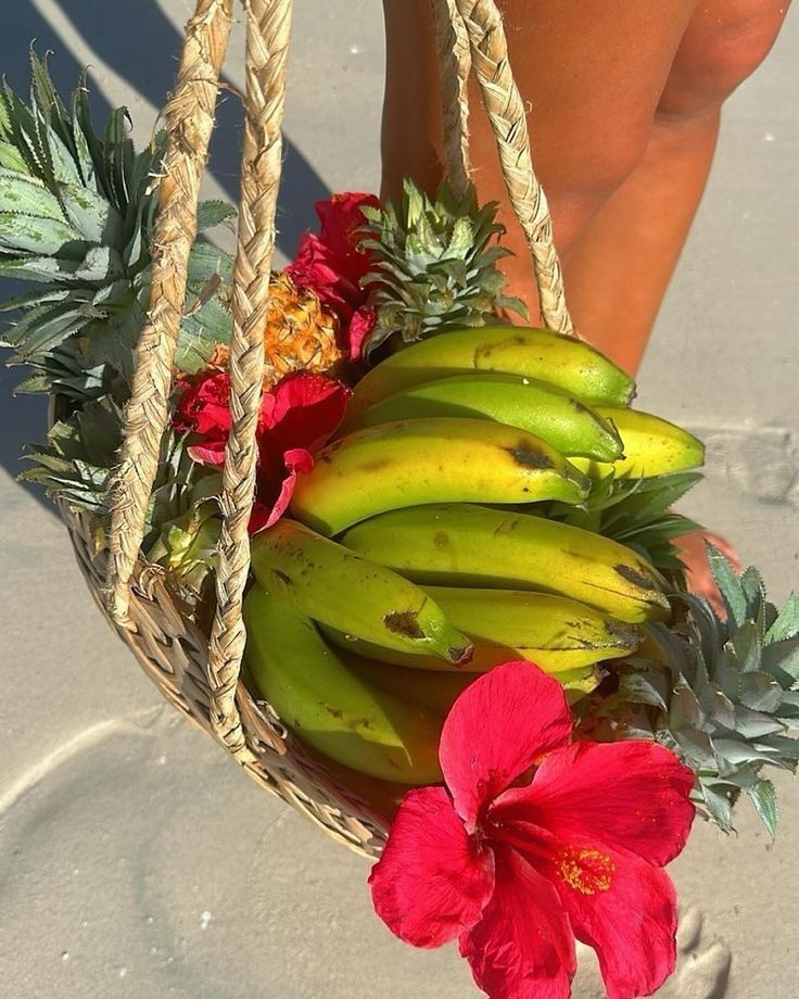 a basket filled with bananas and flowers next to a woman's legs on the beach