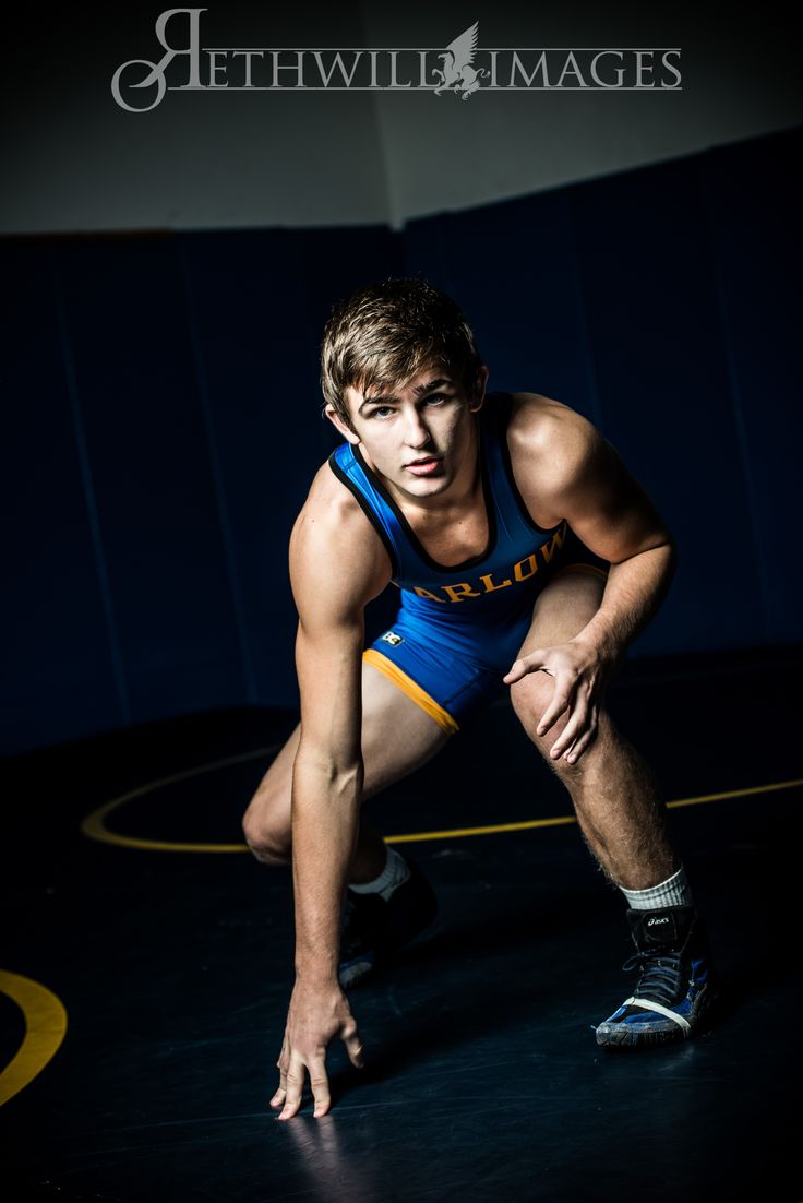 a man in blue and yellow wrestling suit crouching down on the ground with his hands behind his back