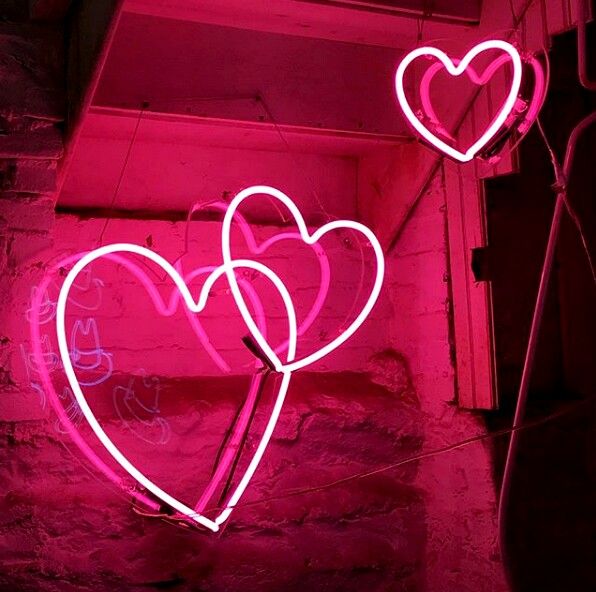 two neon hearts hanging from the side of a wall in front of a pink light