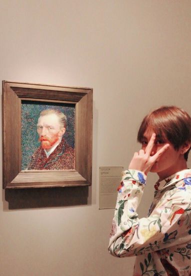 a woman standing in front of a painting with her hand to her face while looking at it