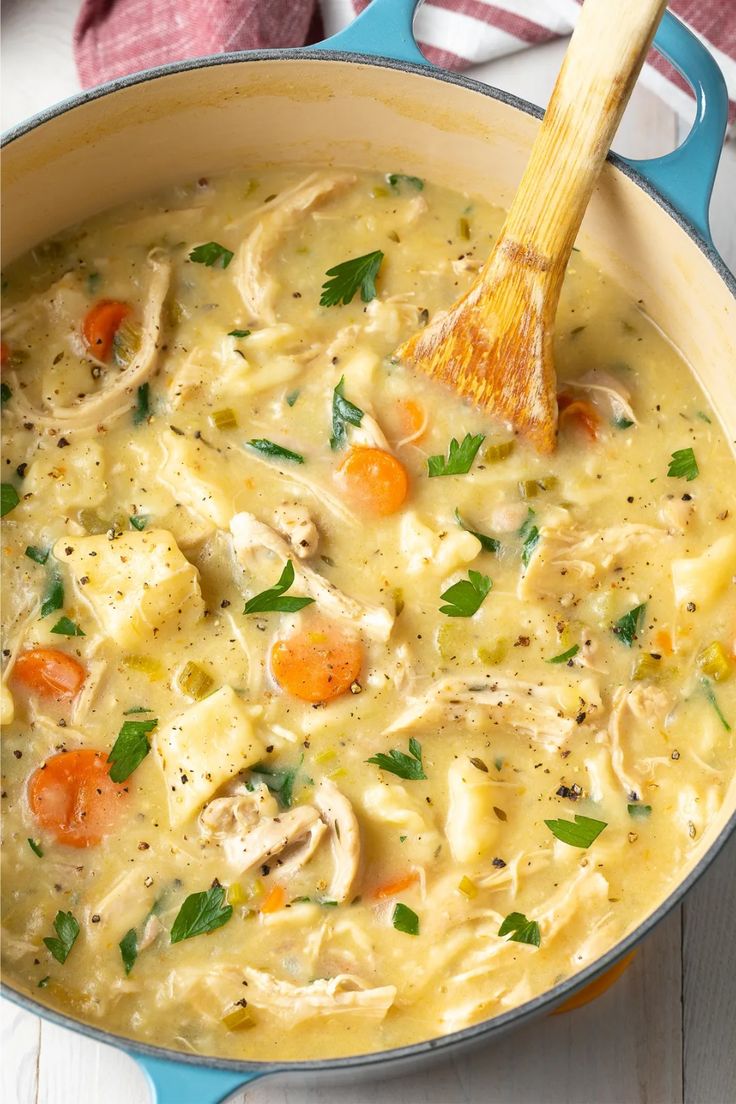 a pot full of chicken and dumpling soup with a wooden spoon