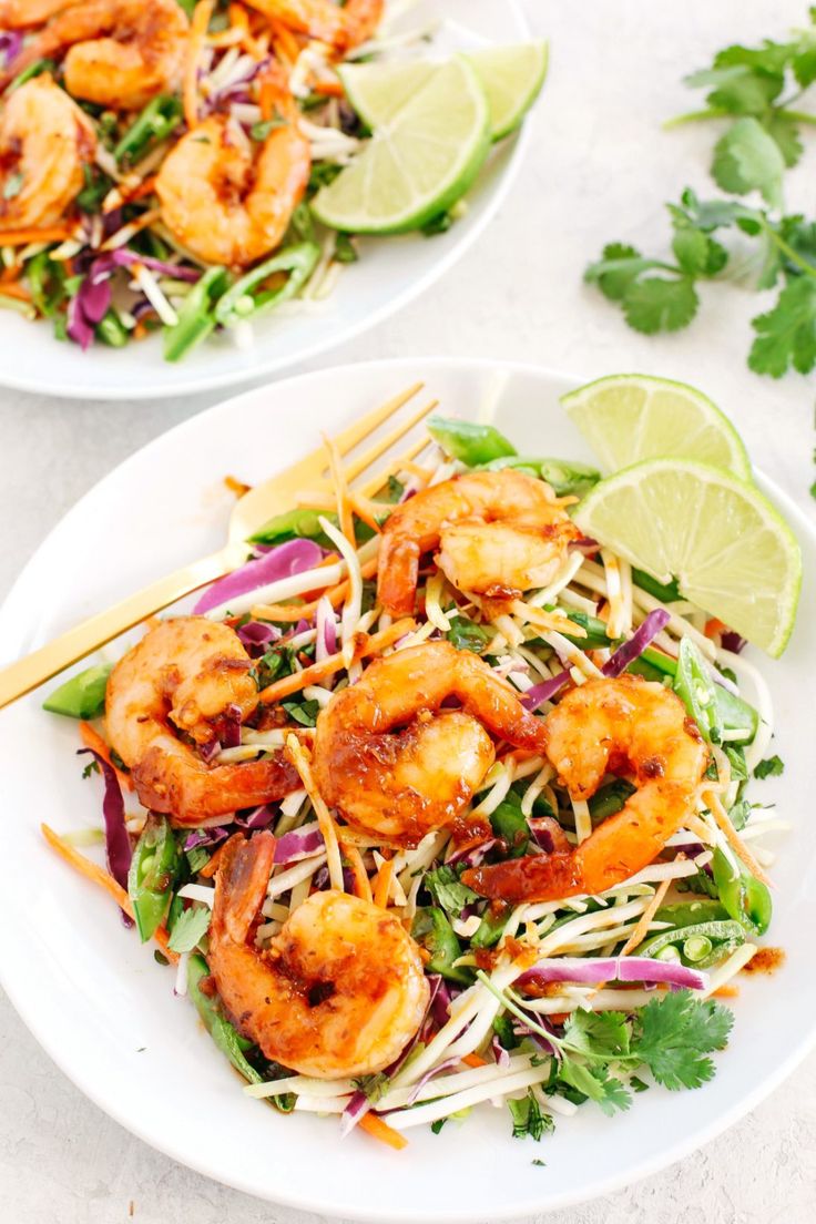 two white plates with shrimp salad and lime wedges on the side next to each other