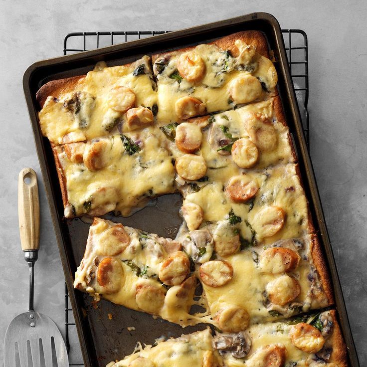 a pan filled with pizza covered in cheese and veggies next to a spatula