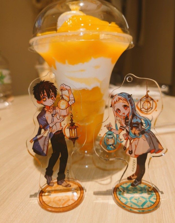 two anime figurines sitting on top of a table next to an orange drink