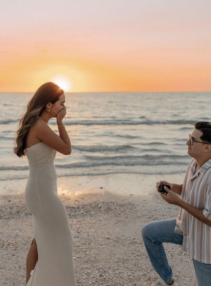 a woman in a white dress standing next to a man on the beach at sunset