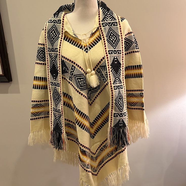 Made In Ecuador- This Beautiful Poncho Is Nwot - No Size Label - Medium 100% Wool Tassel Tie At Neck And 4” Wide Attached Scarf Tassel Trim Hem All Around Cream Background With Black Yellow Brown Orange Pattern Woven Throughout Fun Addition To Your Wardrobe - Keeps You Warm And Finishes Off Your Outfit! Length 38.5” To Longest Point Including Tassels Bin 2 Traditional Long Sleeve Poncho, One Size, Traditional Long Sleeve Poncho One Size, Traditional White Poncho For Fall, Traditional One-size Long Sleeve Cape, Traditional Long Sleeve Cape One Size, One Size Traditional Long Sleeve Cape, Beige Long Sleeve Bohemian Cape, Cream Bohemian Shawl For Fall, Cream Bohemian Poncho For Fall