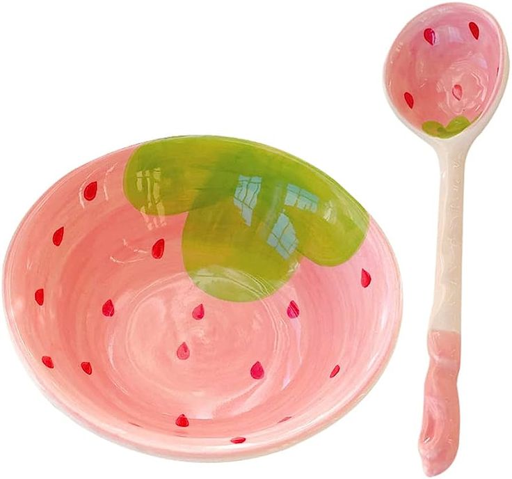 a pink and green bowl next to a plastic spoon on a white surface with polka dots