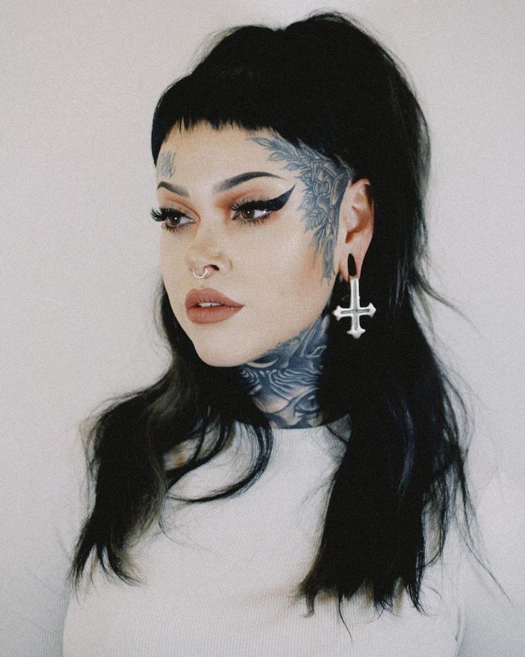 a woman with tattoos and piercings on her face is looking at the camera while wearing earrings