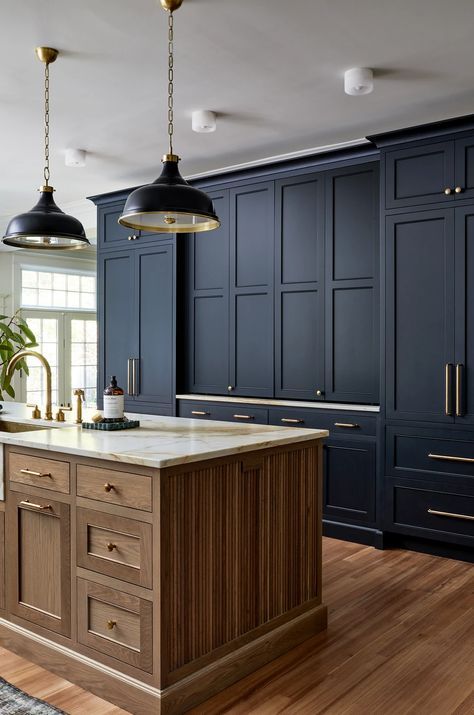 a kitchen with dark blue cabinets and wooden floors, two pendant lights over the island