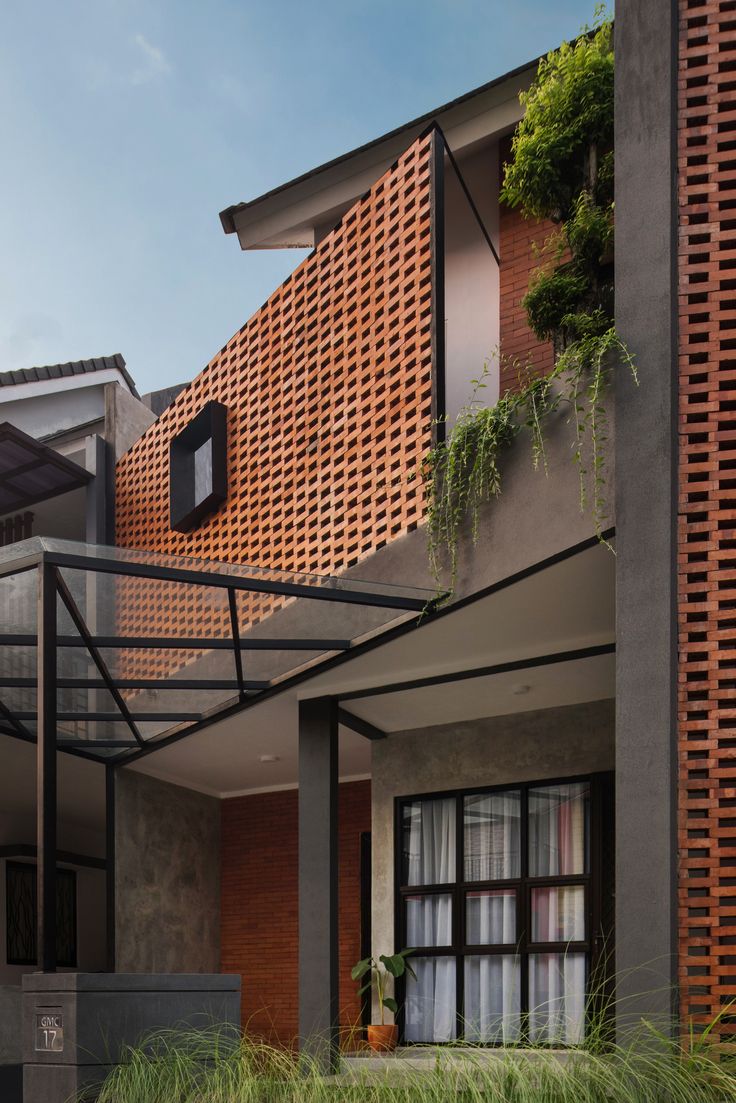 a modern house with red bricks on the side and green plants growing out of the windows