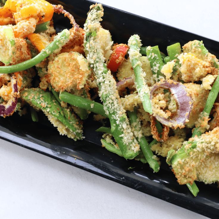 a black tray filled with green beans and other food items on top of a white table