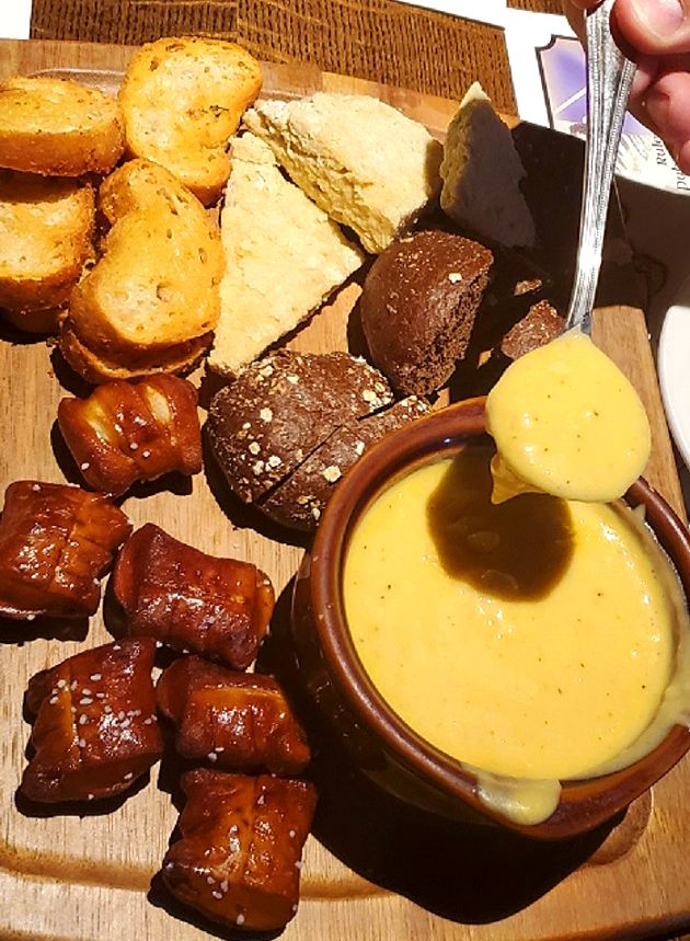 a wooden plate topped with different types of bread and pastries next to a bowl of dipping sauce