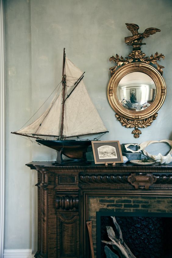 a sailboat sitting on top of a mantle next to a mirror and fire place