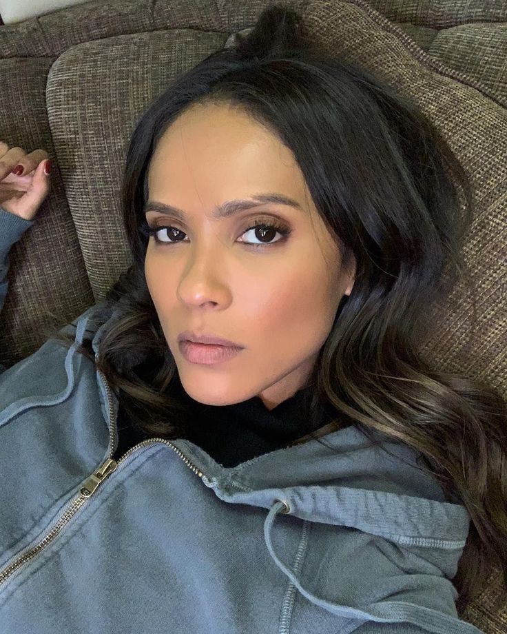 a woman laying on top of a couch wearing a blue jacket and looking at the camera