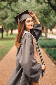 a woman wearing a graduation gown and holding her cap in the air while walking down a path