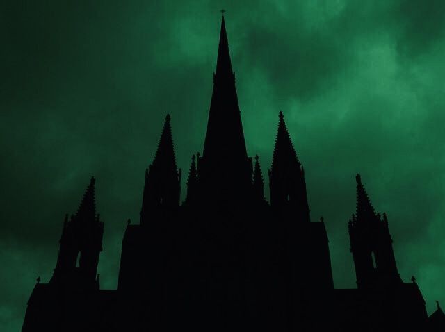 the silhouette of a gothic church against a dark green sky with clouds in the background