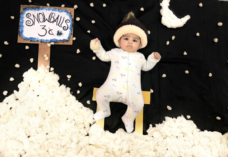 a baby in a snowsuit sitting on top of a pile of white fluffy balls