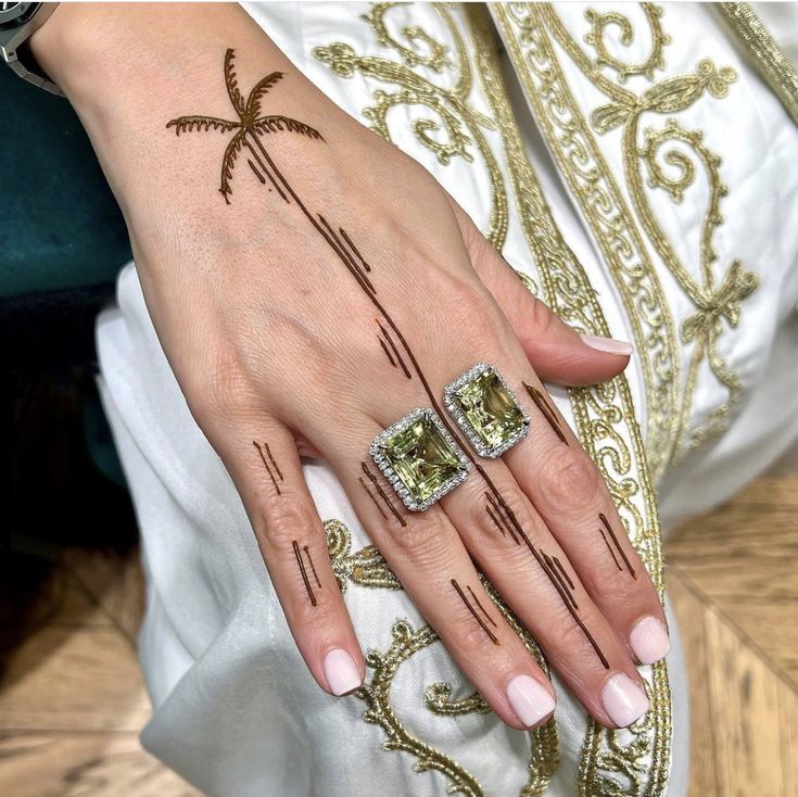 a woman's hand with two rings on it and a palm tree tattooed on the ring finger