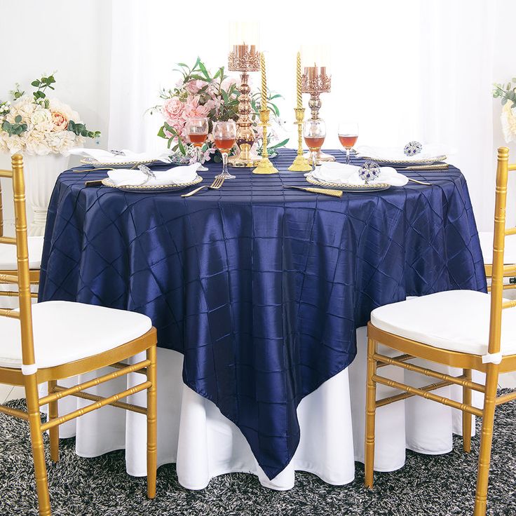 the table is set with two gold chairs and blue cloth on it, along with white linens