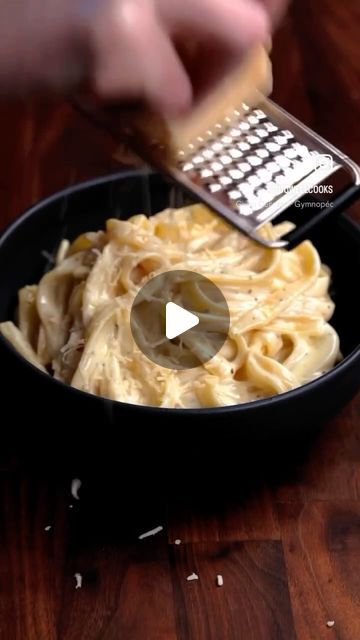 a person using a grater to scoop pasta into a black bowl on a wooden table