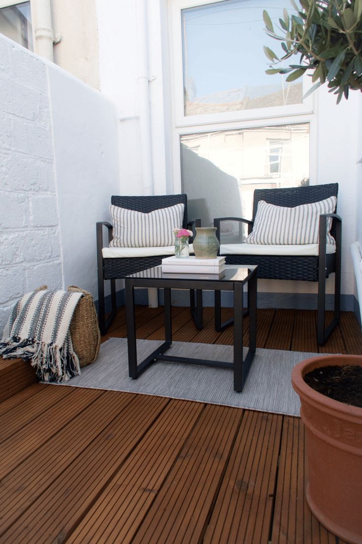 two chairs and a table on a wooden deck with potted plant next to them