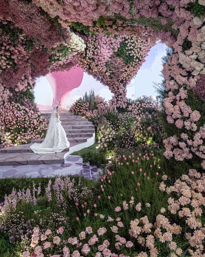 a woman in a white dress is walking through a garden filled with pink and purple flowers