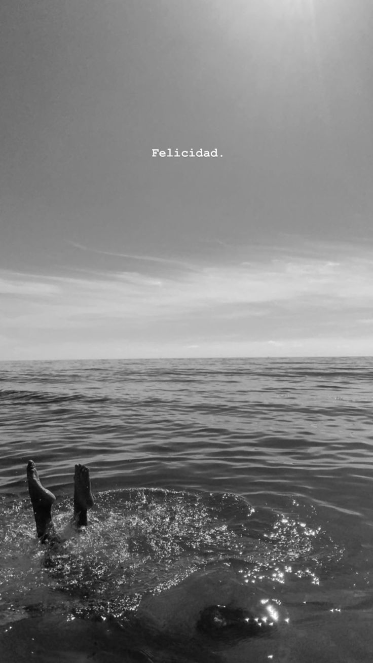 a black and white photo of a person swimming in the ocean with his feet up