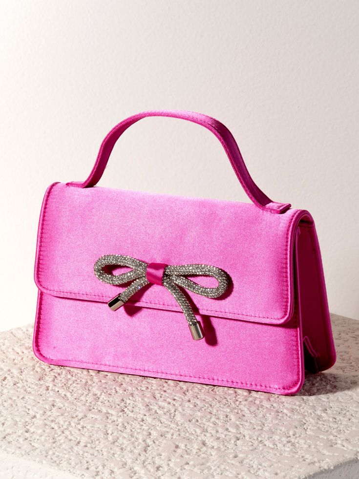 Add a trendy, feminine touch to every outfit with your new favorite bag from Shiraleah - the Bowie Mini Bag. This petite, rectangular purse is made from a sleek satin fabric in a vibrant pink color and features an adorable top handle with a snap closure. The front of the purse is adorned with a sparkling silver bow detail which is sure to turn heads this winter season. Pair with the matching Satin Knotted Headband or other items from Shiraleah to complete your look! Shiraleah is a trend-driven l Elegant Pink Phone Bag With Removable Pouch, Pink Rectangular Baguette Bag For Evening, Pink Rectangular Evening Baguette Bag, Chic Rectangular Clutch With Phone Holder, Chic Rectangular Clutch With Phone Bag, Chic Rectangular Clutch With Mobile Phone Bag, Chic Rectangular Mobile Phone Clutch, Elegant Top Handle Phone Bag As Gift, Gift Top Handle Baguette Bag With Detachable Strap