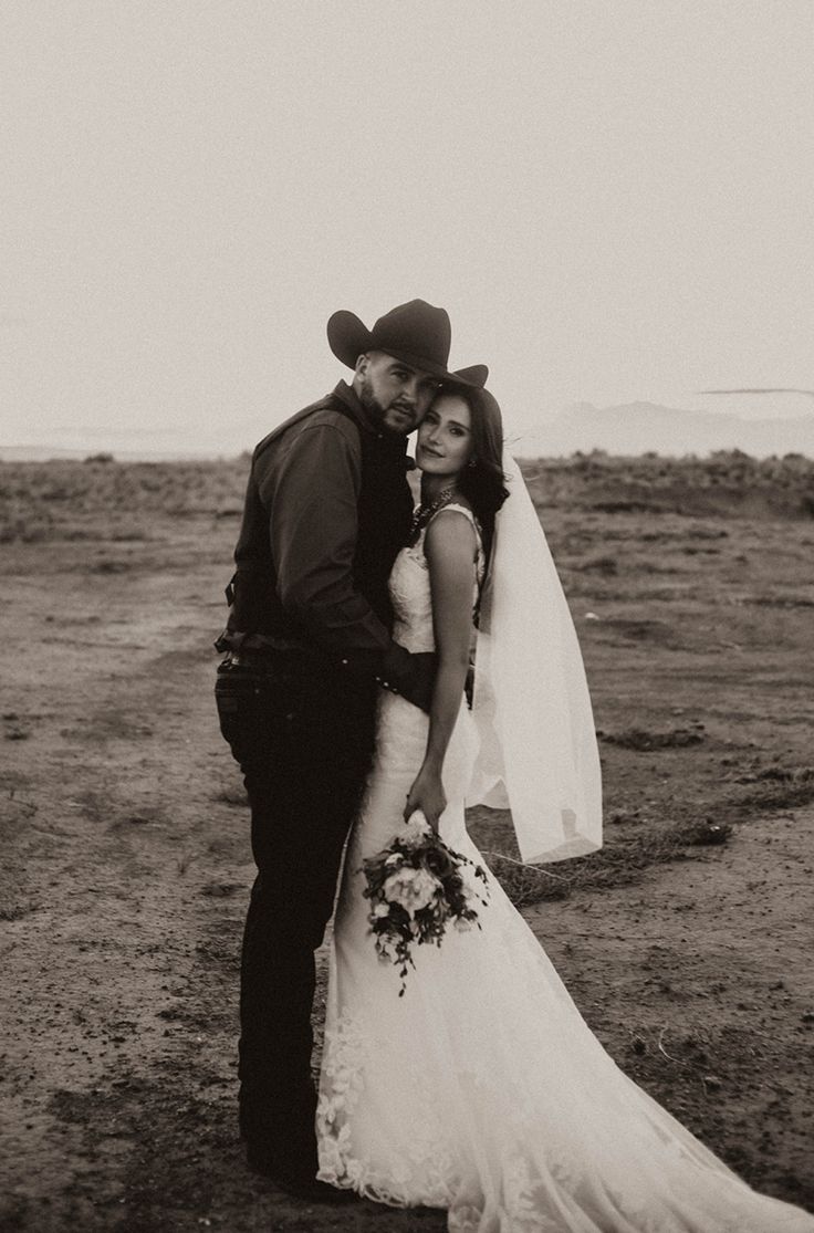 a bride and groom are standing in the middle of an empty field with their heads together