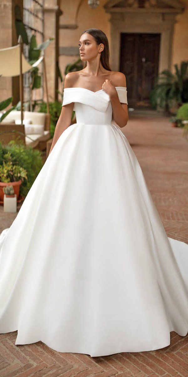 a woman in a white wedding dress standing on a brick walkway with her hands behind her back