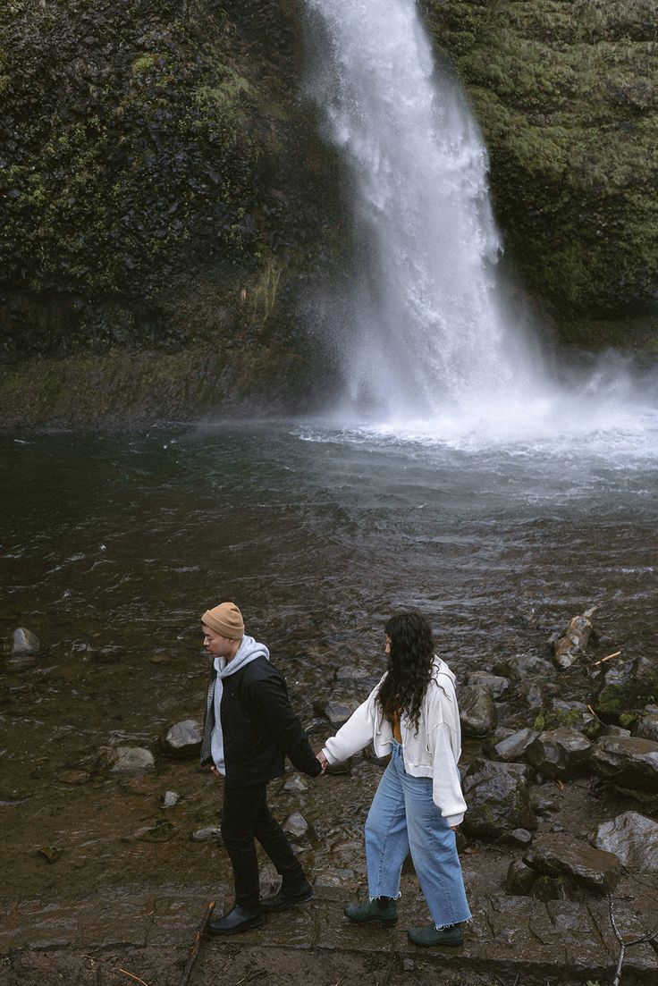 two people holding hands in front of a waterfall