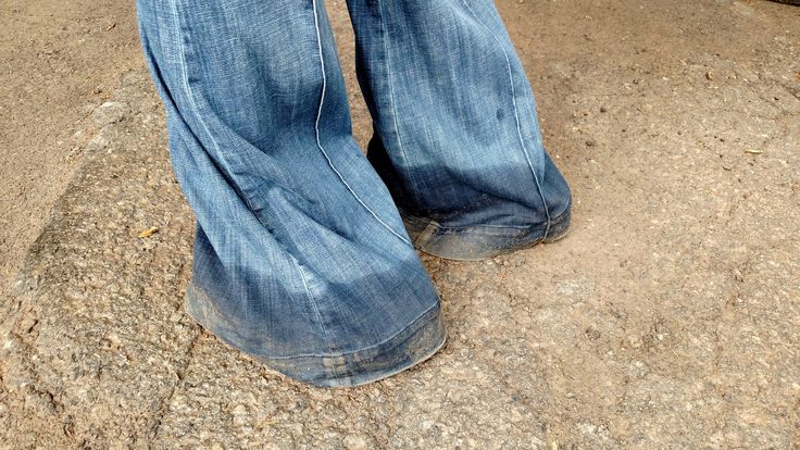 a person standing on the ground with their legs crossed and wearing blue jeans, holding a cell phone