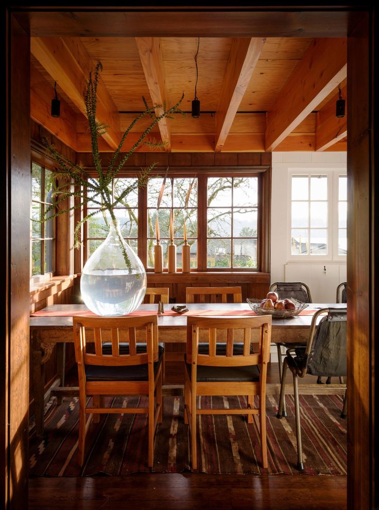 a dining room table with chairs and a vase on it's centerpiece in front of the window