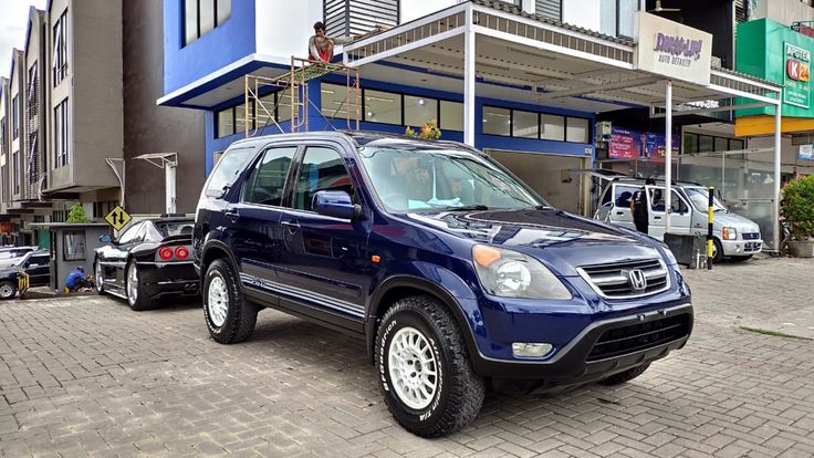 a blue suv parked in front of a building on a brick road next to other cars