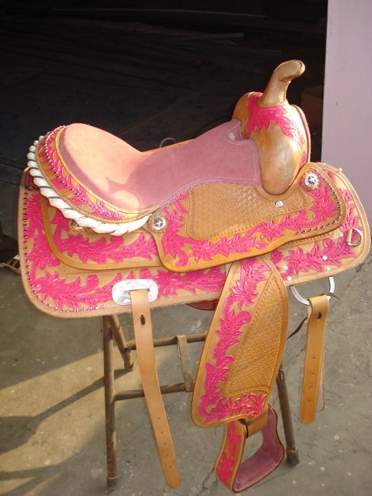 a pink and gold horse saddle sitting on top of a wooden stand